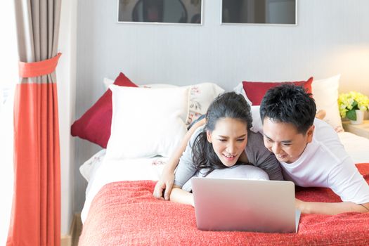 Young Asian Couples using laptop together in bedroom of contemporary house for modern lifestyle concept