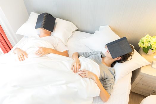 Young Asian Couple laid in a bed reading a book in bedroom of contemporary house for modern lifestyle concept