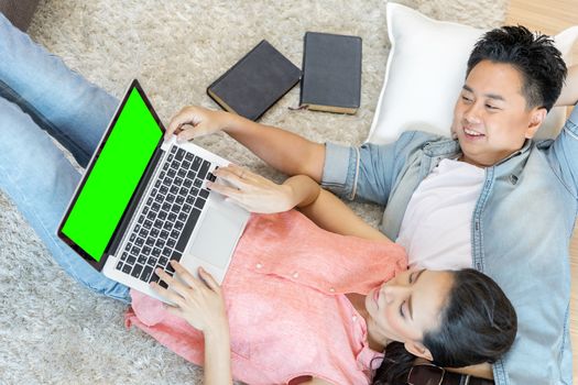 Young Asian Couples lying down and using laptop together in living room of contemporary house for modern lifestyle concept