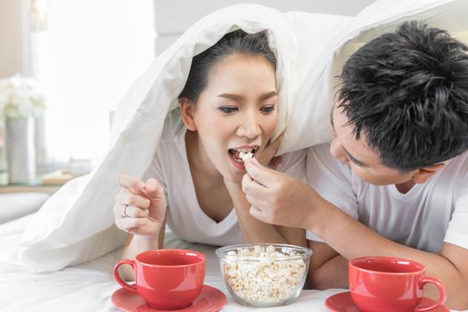 Young Asian Couples having breakfast on bed together in bedroom of contemporary house for modern lifestyle concept