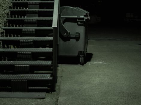 Dark alley with stairs and garbage container