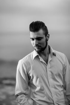 guy with a beard against the sea in the evening in a white shirt, portrait