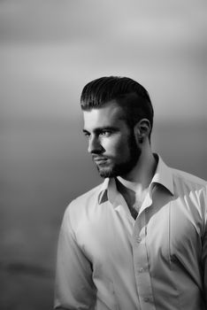 guy with a beard against the sea in the evening in a white shirt, portrait