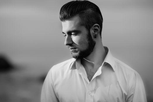 guy with a beard against the sea in the evening in a white shirt, portrait