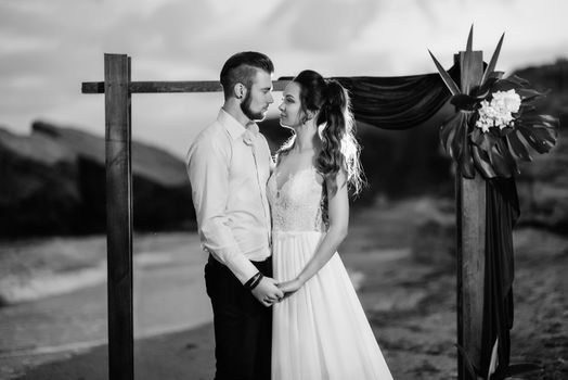 young couple groom and bride with a bouquet in the evening on the beach near the wedding arch