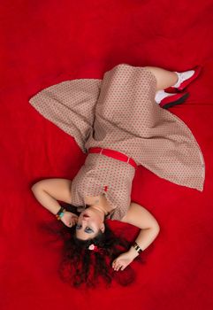 Pinup girl posing on red blacket bed in her bedroom.