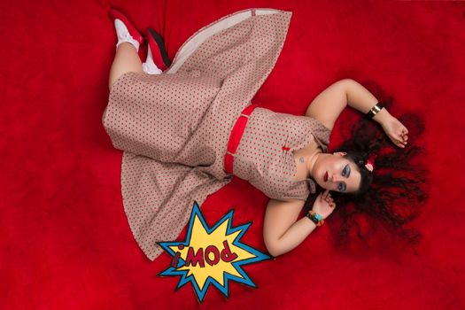 Pinup girl posing on red blacket bed in her bedroom.