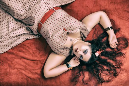 Pinup girl posing on red blacket bed in her bedroom.