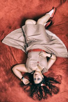 Pinup girl posing on red blacket bed in her bedroom.