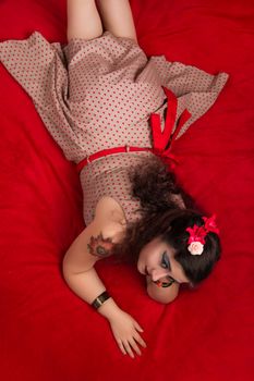 Pinup girl posing on red blacket bed in her bedroom.