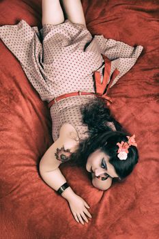 Pinup girl posing on red blacket bed in her bedroom.