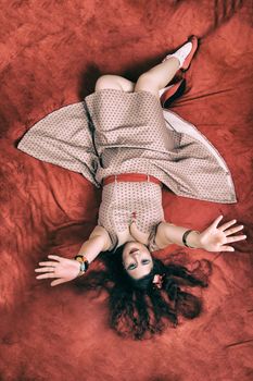 Pinup girl posing on red blacket bed in her bedroom.