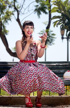 Pinup girl applying lipstick in a beautiful urban park.