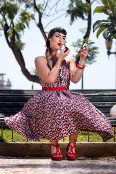 Pinup girl applying lipstick in a beautiful urban park.