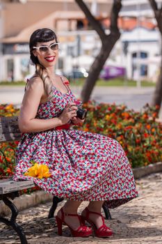 Pinup girl  with dress relaxing in the park, using a vintage camera.