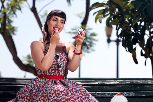 Pinup girl applying lipstick in a beautiful urban park.