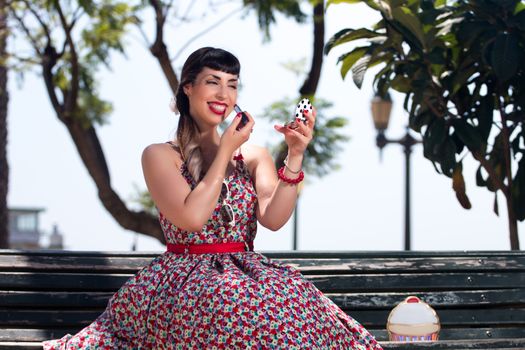 Pinup girl applying lipstick in a beautiful urban park.
