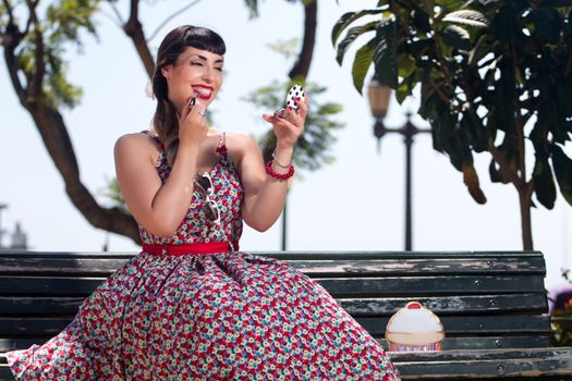 Pinup girl applying lipstick in a beautiful urban park.