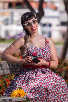 Pinup girl  with dress relaxing in the park, using a vintage camera.