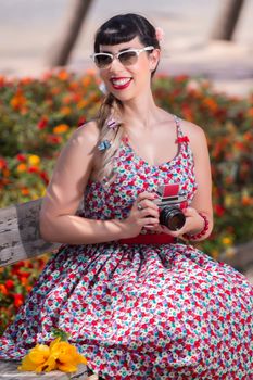 Pinup girl  with dress relaxing in the park, using a vintage camera.