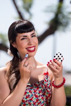 Pinup girl applying lipstick in a beautiful urban park.