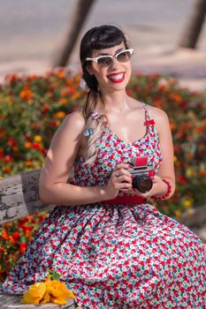 Pinup girl  with dress relaxing in the park, using a vintage camera.