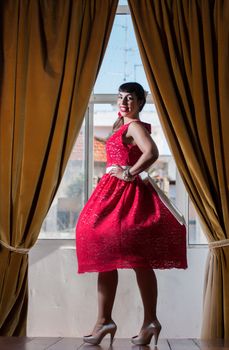 Pinup girl with red dress next to a classic window.