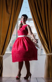 Pinup girl with red dress next to a classic window.