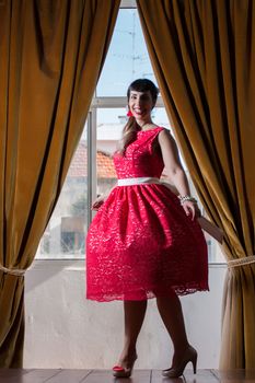 Pinup girl with red dress next to a classic window.