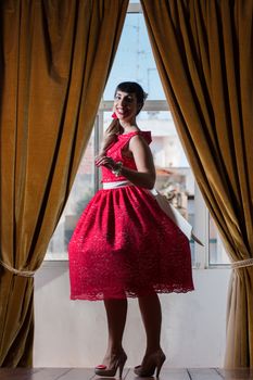 Pinup girl with red dress next to a classic window.
