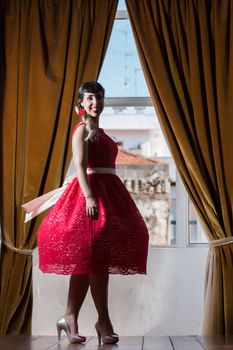 Pinup girl with red dress next to a classic window.