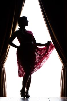 Silhouette of pinup girl with red dress next to a classic window.