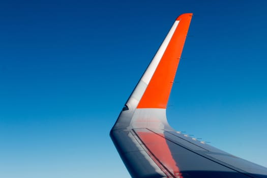 Wing of commercial plane over a clean blue sky.