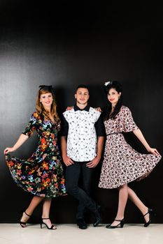 Two woman and a man posing on a vintage style retro clothing.