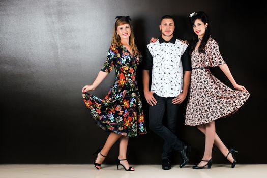 Two woman and a man posing on a vintage style retro clothing.