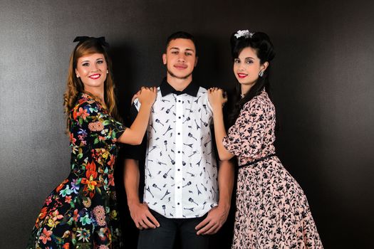 Two woman and a man posing on a vintage style retro clothing.