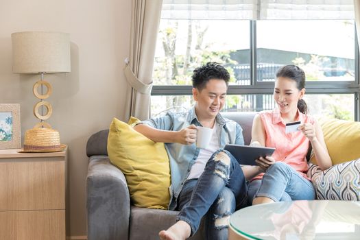 Young Couples using tablet to shopping with credit card in living room of contemporary house for modern lifestyle and e-commerce concept