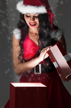 Beautiful woman in Santa Claus style costume looking into glowing Christmas gift box