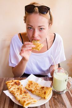 Female tourist eating delicious moroccan brakfast at one of street coffee shops: traditional pancakes with cheese and honey and avocado milkshake.