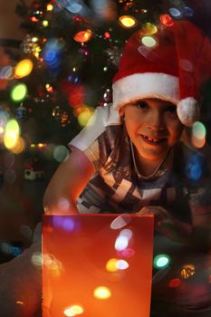 Happy little boy opens his magic glowing christmas gift near decorated christmas tree