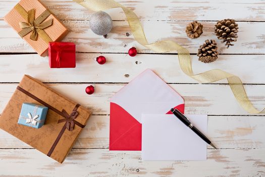 Christmas letter and pen over a rustic wooden table with presents, decorations and pine cones