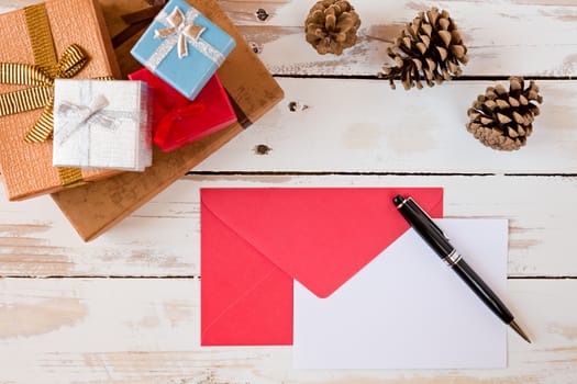Closeup of Christmas letter and pen over a rustic wooden table with presents and pine cones
