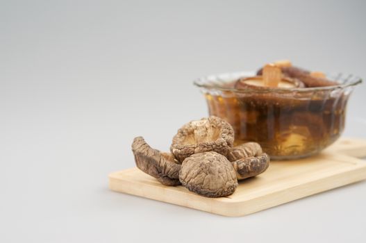 Shiitake mushroom and soak  mushroom in cup place on wooden chopping board with white background and copy space.