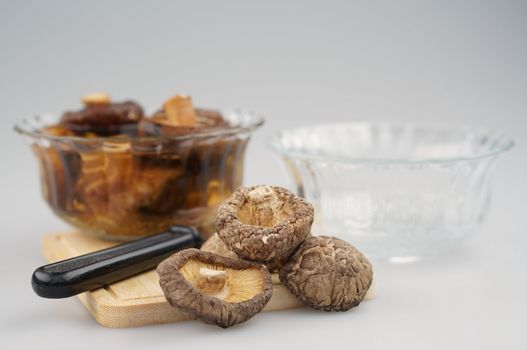 Dry Shitake mushroom or lentnus edodes and knife place on chopping board have blur mushroom soak and bowl as background photography with white background.