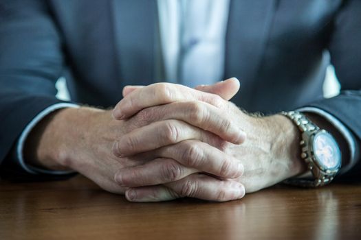 Close-up of businessman keeping hands with fingers crossed on the table