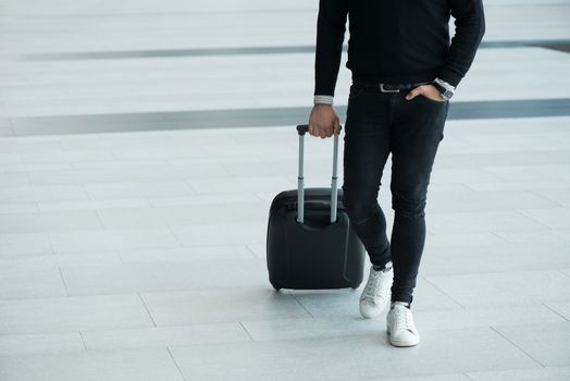 Man walking with wheeled bag at airport terminal and talking on phone