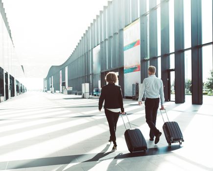 Business people in formal clothing walking in airport terminal with suitcases