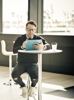 Mature man sitting in cafe of modern office building and using tablet