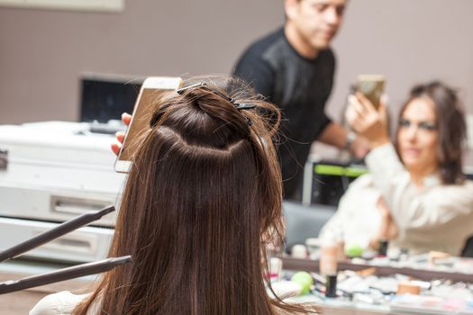 Stylist Using Flat Iron on Hair of Female Client Sitting in Salon Chair