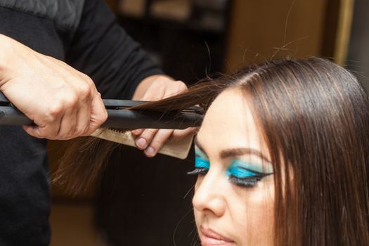 Stylist Using Flat Iron on Hair of Female Client Sitting in Salon Chair